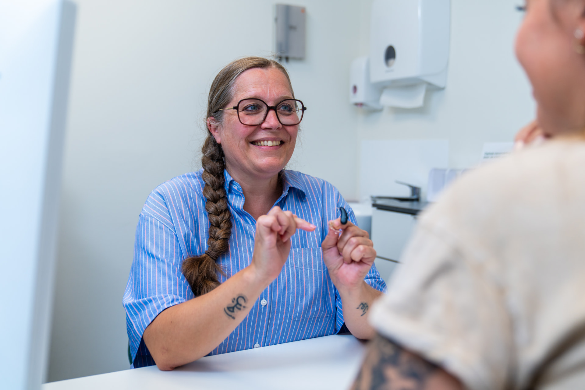 Een audicien legt een client rustig uit hoe een gehoorapparaat werkt